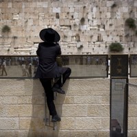 Ortodoksyjny Żyd opierając się o uchwyty do wieszania flag obserwuje modlących się przy Ścianie Płaczu [PAP/EPA/JIM HOLLANDER]