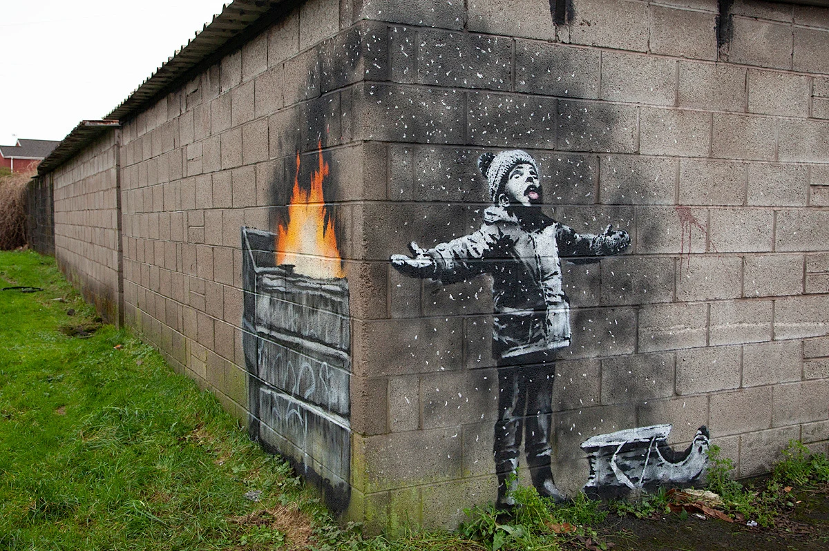 Ikona street artu Banksy pokazał na Instagramie swoje najnowsze dzieło - graffiti na jednym z garaży w walijskim Port Talbot, sercu brytyjskiego przemysłu stalowego. Pojawiły się już interpretacje, że to komentarz artysty do problemu zanieczyszczenia powietrza. Na ceglanej, pomalowanej na biało ścianie garażu widać chłopca z sankami, który podnosi twarz do góry i na wyciągnięty język próbuje złapać lecące z nieba płatki śniegu. Gdy jednak zmienimy perspektywę i przeniesiemy się za róg budynku, na sąsiedniej ścianie zobaczymy, że unoszące się w powietrzu drobiny to resztki odpadów z palącego się śmietnika.