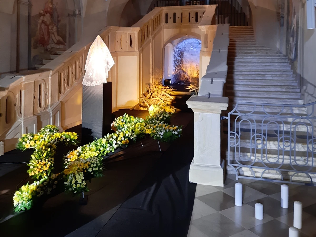 Porozrzucane w nieładzie drewniane krzyże i żółto-niebieskie podświetlenie, a wokół kwiaty - tak wygląda w tym roku Grób Pański w klasztorze Ojców Pijarów w Krakowie. Od wielu lat aranżowane tam groby nawiązują do aktualnej sytuacji społecznej.