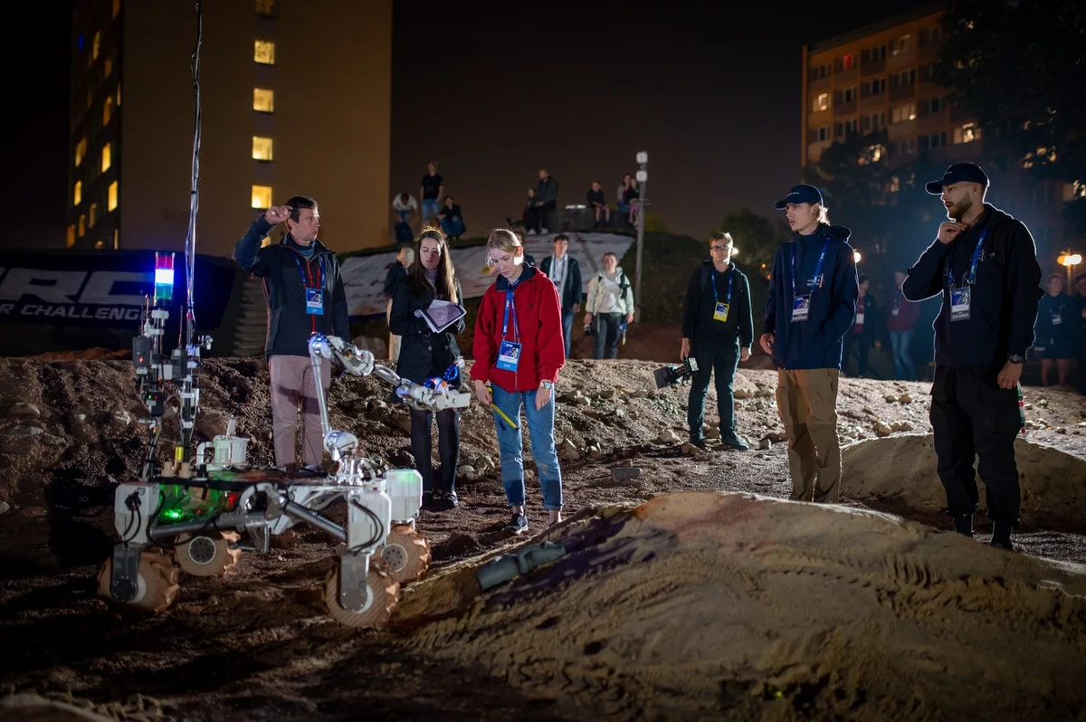 8. edycja European Rover Challenge nie przestaje zaskakiwać. Minionej nocy mieszkańcy Kielc mogli obserwować zmagania łazików marsjańskich po raz pierwszy także po zmroku. Drużyny uczestniczące w zawodach wykonywały zadania związane z pobieraniem próbek i przemieszczaniem się po torze marsjańskim przy sztucznym oświetleniu. Decyzja organizatorów, by prowadzić rywalizację także w nocy, to innowacja w formule zawodów, która drużynom z całego świata daje okazję przetestowania swoich łazików w nowych okolicznościach. Za uczestnikami już pierwsze konkurencje, które pokazują, w czym dany zespół się wyróżnia, a nad czym powinien jeszcze popracować.