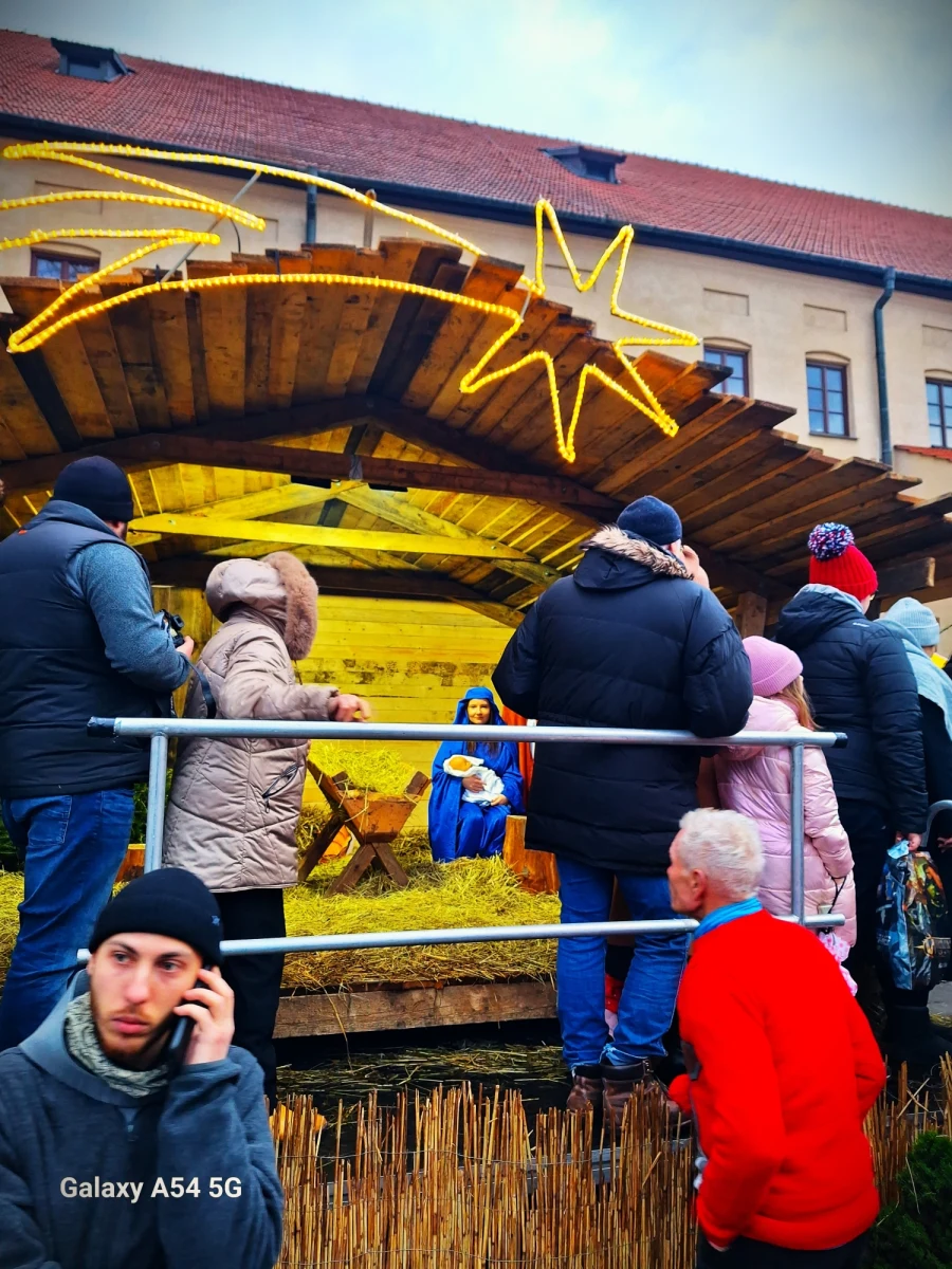 I ja tam byłem, pastorałki z wiernymi śpiewałem i razem z Magdaleną Wojtoń prezentowałem franciszkańskie fakty historyczne. Jednak to był taki nasz skromny "kwiatek" św. Franciszka do bogatego artystycznego "kożucha". W jego muzyczno-tanecznym cieple ogrzewali się przed Bazyliką Franciszkanów i Oknem Papieskim w Krakowie licznie zgromadzeni ludzie, w większości rodziny z dziećmi.  Jak mogliśmy przeczytać w depeszy: "w tegorocznej jubileuszowej 'żywej szopce' w Krakowie kolędy i pastorałki zaśpiewał Marek Piekarczyk, wokalista legendarnej grupy TSA i trener polskiej edycji The Voice of Poland. Na scenie przy Franciszkańskiej pojawili się ponadto: Magda Steczkowska, 'hulajdusza', 'Jakubowe Muszelki', 'Promyczki Dobra', 'Kwartet C.D.N.' oraz franciszkański zespół 'Fioretti'. Jak co roku w Wigilię i Święta Bożego Narodzenia (24-26 grudnia 2023 r.) obowiązkowo byli na skwerze: Święta Rodzina, zwierzęta, jasełka. Było wspólne kolędowanie i tańce. Franciszkanie serdecznie zapraszają w tych dniach do sąsiadującej z ,żywą szopką' bazyliki św. Franciszka. 'Jeśli naprawdę chcemy spotkać żywego Jezusa, to właśnie tam, na ołtarzu podczas mszy św. rodzi się On. W tym momencie, kiedy kapłan wyciąga ręce nad chlebem i winem i przyzywa Ducha Świętego, aby dary te stały się Ciałem i Krwią Chrystusa' – tłumaczą zakonnicy. Pierwszą żywą szopkę wystawił św. Franciszek z Asyżu w Greccio 800 lat temu, 24 grudnia 1223 r. Ponad ćwierć wieku temu krakowscy franciszkanie zwyczaj ten przeszczepili do Polski." Przepisałem oficjalny artykuł. A teraz zapoznajcie się z historią zaprezentowaną przez Magdę i mnie.       