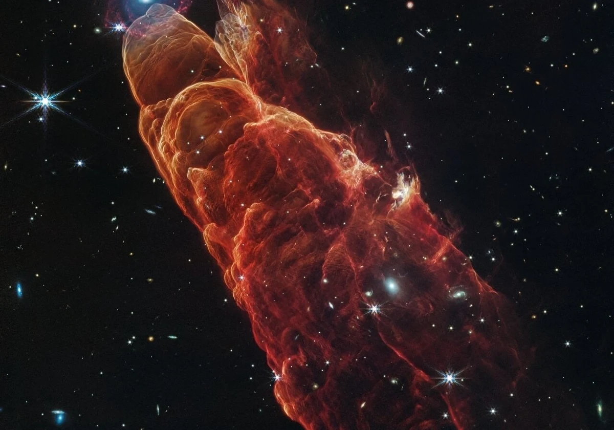 Naukowcy korzystający z Teleskopu Kosmicznego Jamesa Webba opublikowali niezwykłe zdjęcie dwóch odmiennych światów astronomicznych. Widać na nim względnie blisko nas położony wyrzut materii Herbig-Haro 49/50 - nazywany Kosmicznym Tornadem - oraz idealnie umiejscowioną, znacznie bardziej oddaloną spiralną galaktykę. Zdjęcie, będące połączeniem obserwacji z kamery NIRCam (Near-Infrared Camera) i instrumentu MIRI (Mid-Infrared Instrument) Teleskopu Webba, dostarcza wysokiej rozdzielczości obrazu, pokazującego wyrzuty materii produkowane przez strumienie plazmy emitowane przez formującą się gwiazdę. Teleskop Webba otwiera nowe możliwości zrozumienia, jak aktywność tych strumieni - zwanych dżetami - może wpływać na otoczenie młody gwiazd.