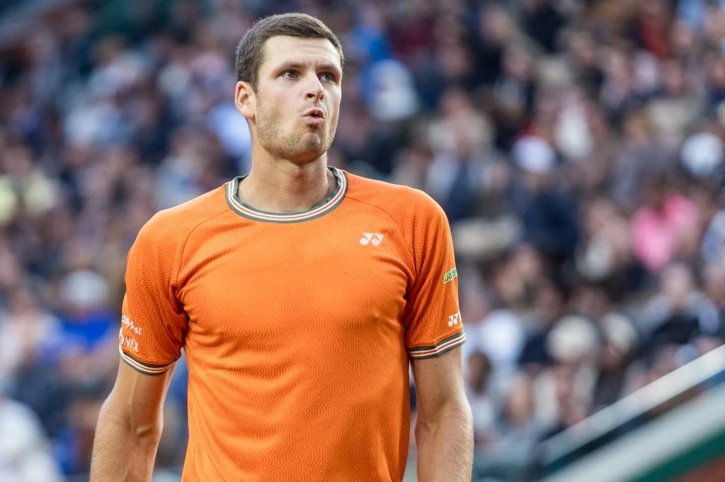 Mężczyzna w pomarańczowej koszulce sportowej stoi na korcie tenisowym, w tle rozmyta publiczność. Mężczyzna w pomarańczowej koszulce sportowej stoi na korcie tenisowym, w tle rozmyta publiczność.