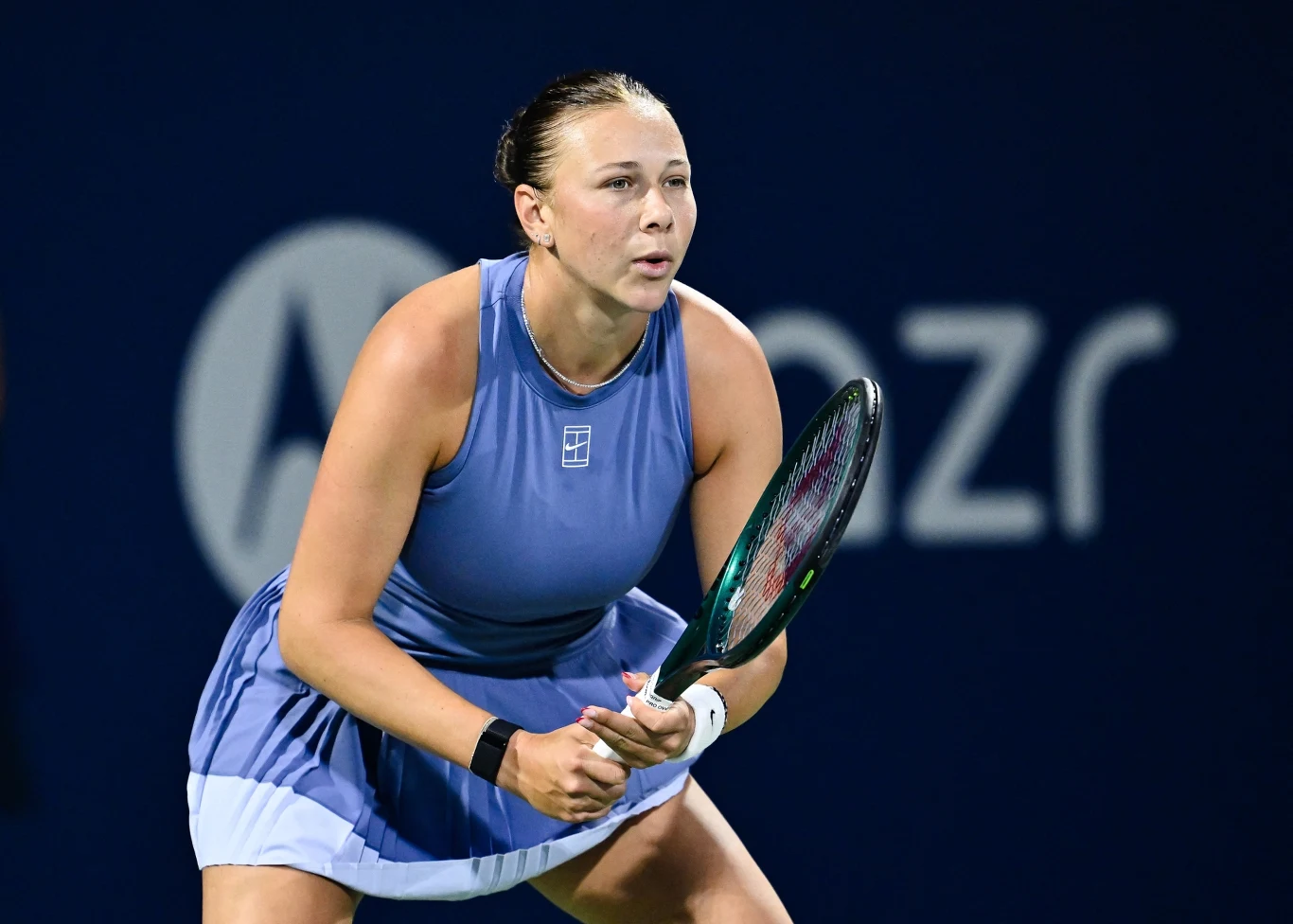 Zawodniczka tenisa w fioletowej sukience sportowej skupiona w trakcie meczu na korcie tenisowym, z rakietą w dłoniach i gotowością do odbioru piłki