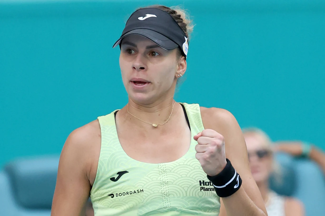 Kobieta w sportowym stroju, z daszkiem na głowie, zaciśniętą pięścią podkreślającą emocje, stoi na tle rozmytego widza podczas zawodów sportowych.