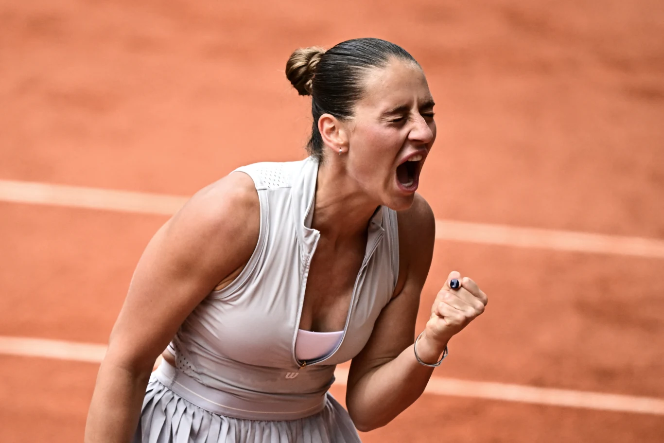 Marta Kostiuk Kobieta ubrana w sportową sukienkę z zaciśniętą pięścią wyraża silne emocje na korcie tenisowym.