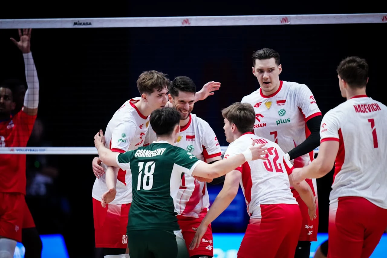 Grupa polskich siatkarzy ubranych w biało-czerwone stroje świętuje zdobycie punktu, obejmując się i okazując radość na boisku.