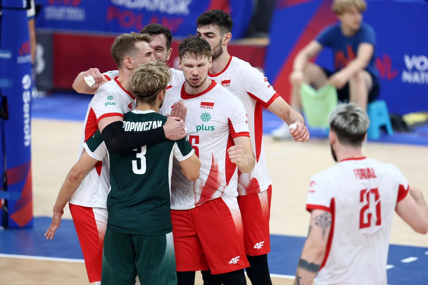 Grupa polskich siatkarzy w biało-czerwonych strojach świętuje zdobycie punktu na boisku podczas meczu, obejmując się i okazując radość.