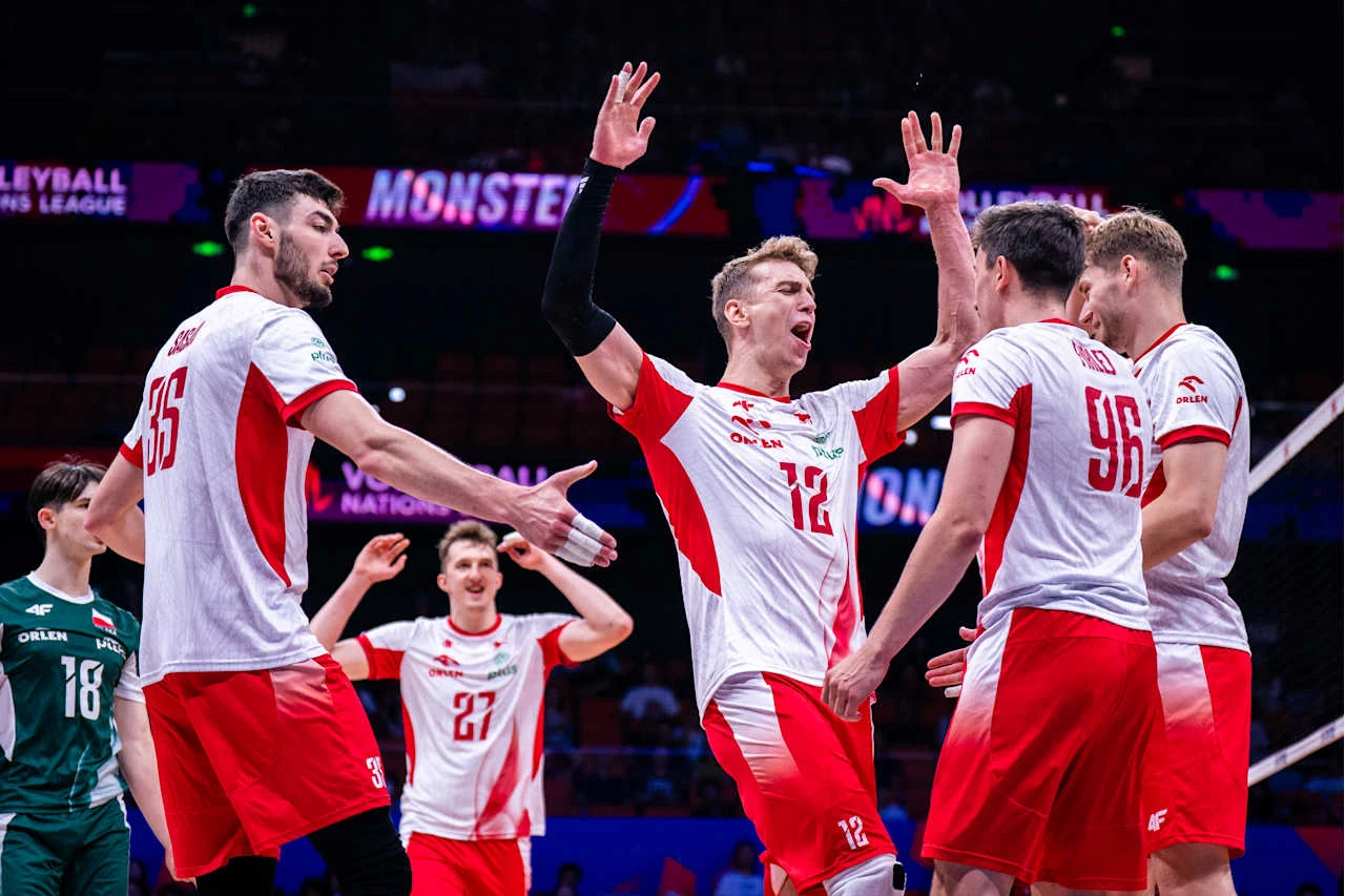 Grupa polskich siatkarzy w biało-czerwonych strojach celebruje zdobyty punkt podczas meczu na hali sportowej.