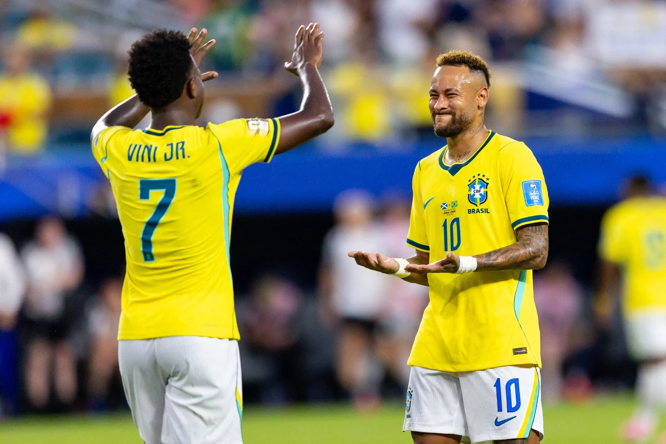 Dwóch piłkarzy reprezentacji Brazylii w żółtych koszulkach podczas celebracji na boisku, jeden z nich pokazuje numer 7 na plecach, a drugi wykonuje charakterystyczny gest rękami.