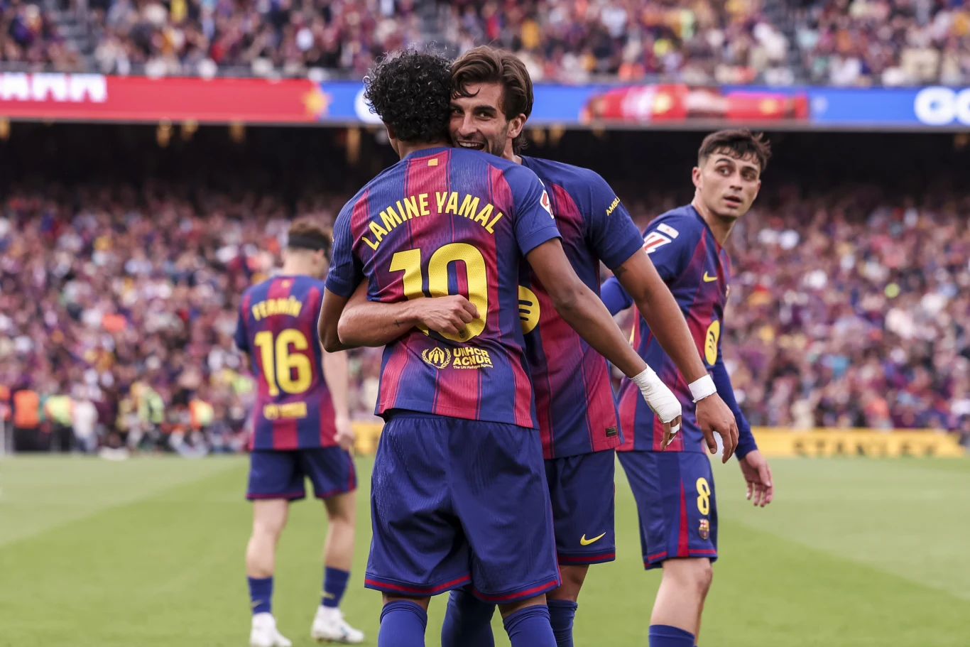 Piłkarze drużyny FC Barcelona w granatowo-bordowych strojach świętują bramkę na murawie stadionu, obejmując się i uśmiechając, na pierwszym planie zawodnik z numerem 10 i napisem Lamine Yamal. Piłkarze drużyny FC Barcelona w granatowo-bordowych strojach świętują bramkę na murawie stadionu, obejmując się i uśmiechając, na pierwszym planie zawodnik z numerem 10 i napisem Lamine Yamal.