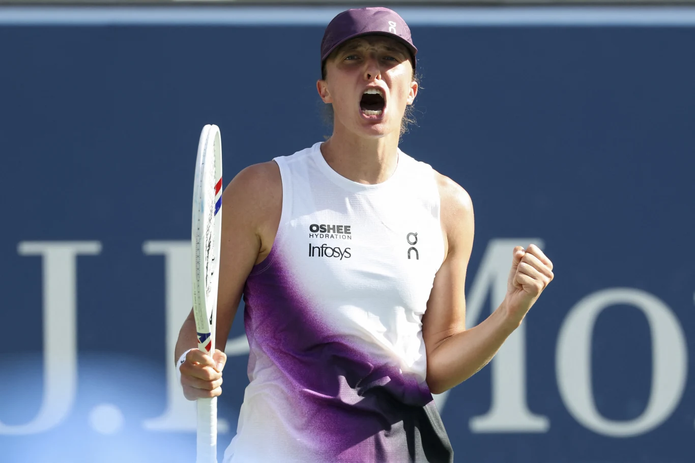 Iga Świątek Tenisistka w sportowej koszulce z rakietą w dłoni oraz zaciśniętą pięścią wyraża intensywne emocje podczas meczu na korcie.
