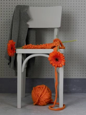 Styl nastrojowy. Gerbera. Kwiat zrobiony na drutach, czy to jakiś żart? Z łatwością można się pomylić. Pomarańczowy kolor włóczki i kwiatu idealnie się ze sobą zlewają. Ten wyraźny kolor tworzy wspaniały kontrast z otaczającą szarością. 