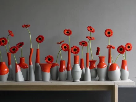 Styl nowoczesny. Gerbera. Ta aranżacja idealnie pasuje do muzeum sztuki współczesnej. Szaro-czerwone wazoniki odznaczają się na tle szarej ściany. Jednakowy kształt gerber i wyrafinowany czerwony kolor nadają kompozycji wykwintny charakter. 