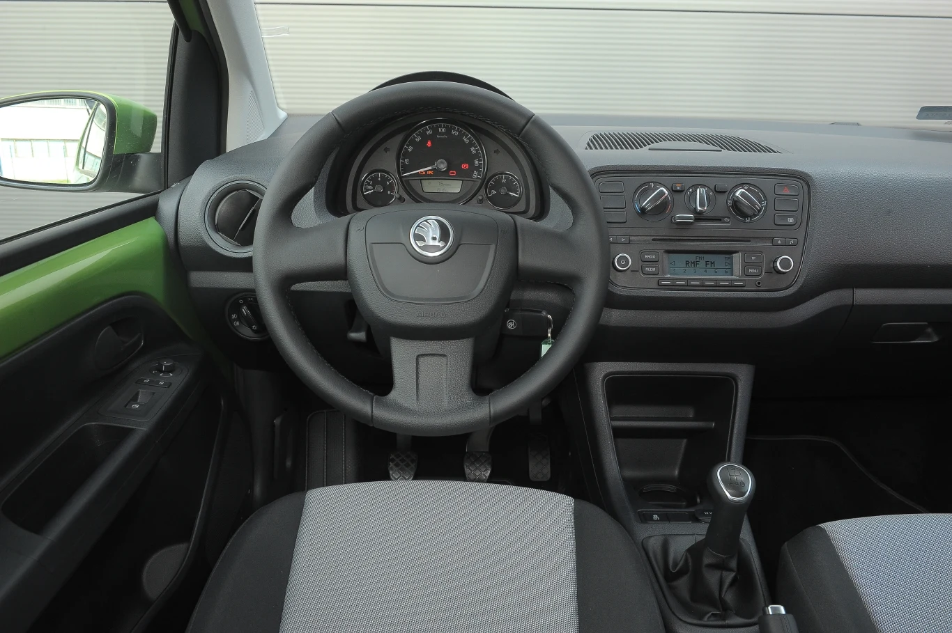 Prosty kokpit Citigo w mniej ciekawym, czarnym wydaniu. Kierownica z innych modeli Skody tutaj wydaje się za duża. Zbyt mały jest z kolei obrotomierz (lewy wskaźnik). Na lewych i prawych drzwiach umieszczono tylko po jednym przycisku do obsługi szyb, więc jeśli kierowca zechce opuścić tę prawą, musi sięgnąć do dalszego przycisku. Nieco rażą nieosłonięte blachy na drzwiach – nawet w autach tego segmentu zdarzają się one coraz rzadziej. Tworzywa są niezłe, a ich spasowanie – bardzo dokładne.