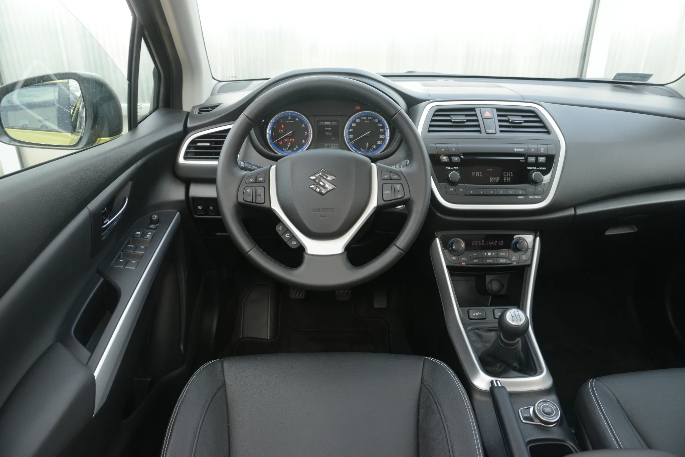 Suzuki SX4 S-Cross 1.6 VVT Comfort: srebrne wstawki nie są w stanie ożywić wnętrza. Deska rozdzielcza wygląda skromnie, za to jest banalna w obsłudze. Niestety, spasowanie oraz jakość materiałów pozostawiają wiele do życzenia.