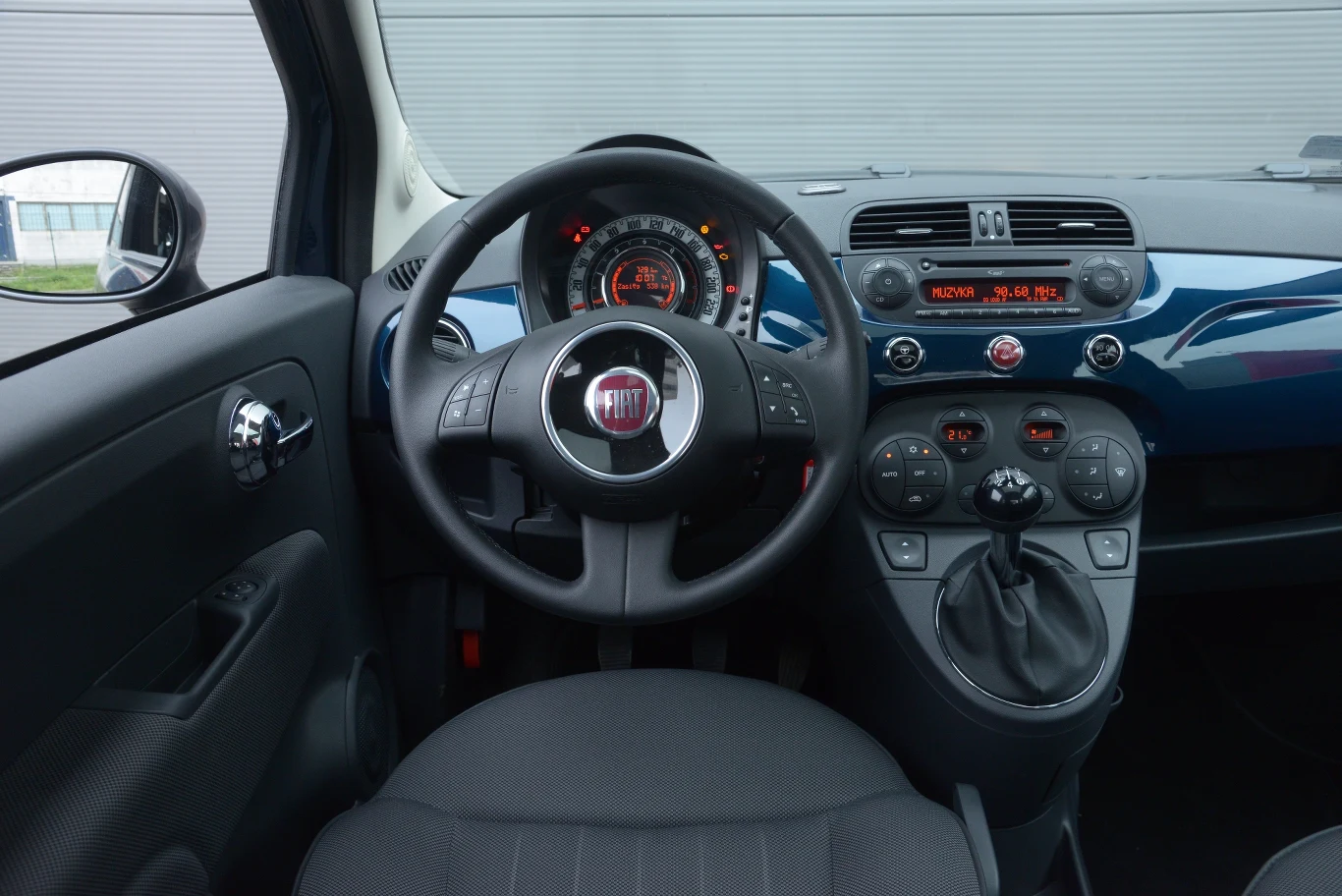 Fiat 500 1.2 POP z klimatyzacją: styl retro w dobrym tego słowa znaczeniu. Wysoko umieszczona dźwignia biegów sama wpada w rękę. Kierownica ma tylko pionową regulację, ale bez problemu da się znaleźć dogodną pozycję do jazdy.