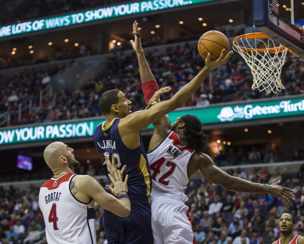 "Pelikan" Alexis Ajinca w ataku na kosz Wizards. Próbuje go zatrzymać Nene, a akcji przygląda się Marcin Gortat