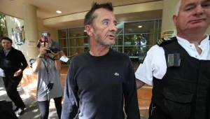 Phil Rudd w asyście policjanta opuszcza budynek sądu - fot. Joel Ford