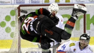 Hokeista GKS Tychy Jurii Kuzin (L) strzela na bramkę Bryana Pittona (w głębi) z Ciarko PBS Bank KH Sanok 