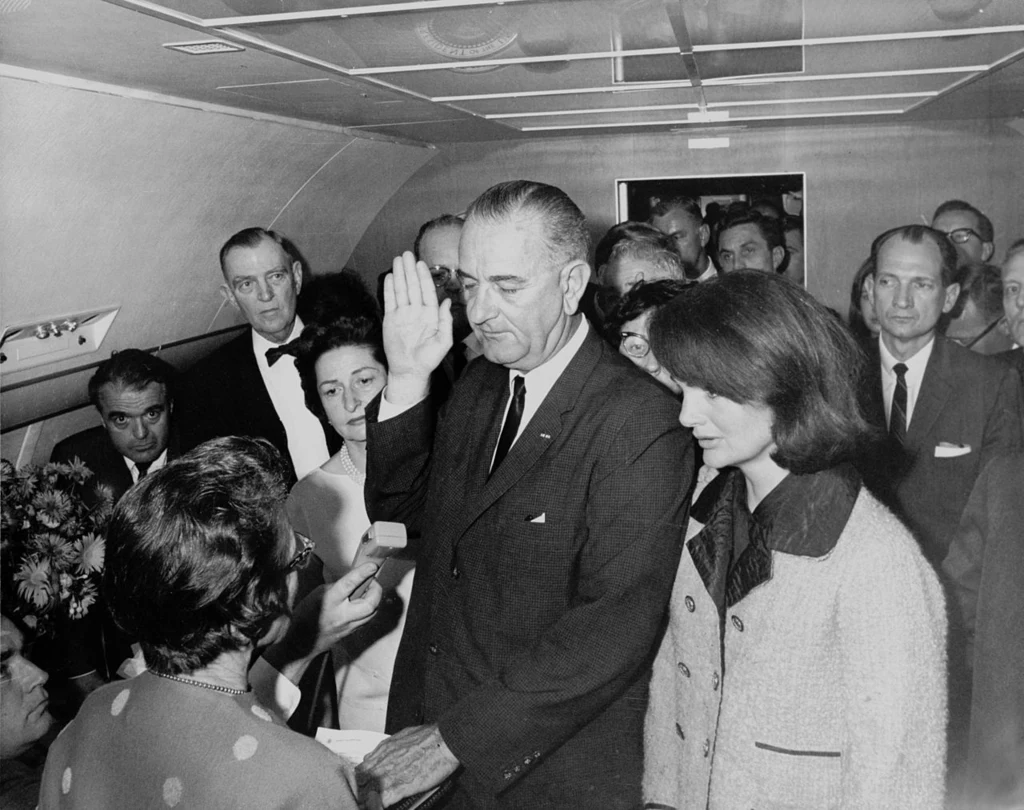 Lyndon B. Johnson w czasie składania przysięgi prezydenckiej po śmierci Johna F. Kennedy'ego. U jego boku stoi Jakie Kennedy