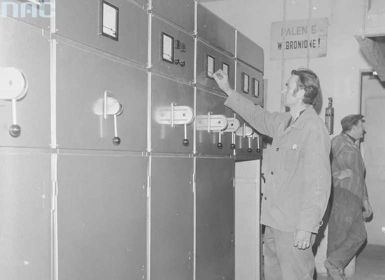 Pracownik przy rozdzielni elektrycznej. Widoczne mierniki tablicowe (zdjęcie ilustracyjne)