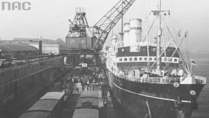 Statek pasażerski SS "Kościuszko" widoczny od strony dziobu podczas przeładunku w porcie w Gdyni. Widoczne portowe urządzenia przeładunkowe oraz wagony kolejowe