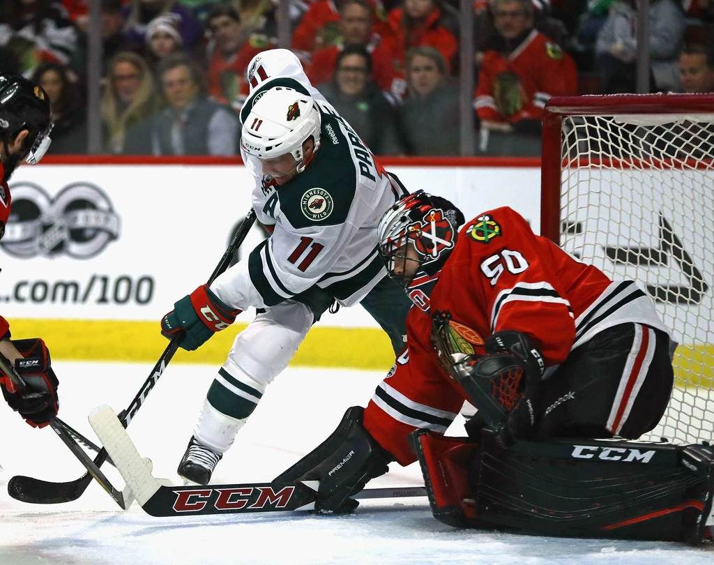 Corey Crawford z Chicago Blackhawks broni strzał Zacha Parise z Minnesota Wild