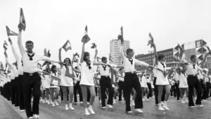 Młodzież wykonująca układy gimnastyczne z chorągiewkami podczas przemarszu ulicą Marszałkowską w Warszawie