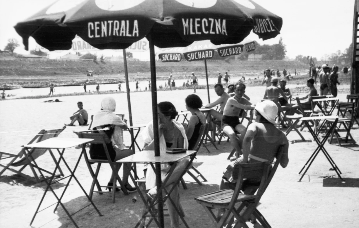 Plażowicze podczas wypoczynku przy stolikach pod parasolami. Plaża Towarzystwa Uniwersytetu Robotniczego w Krakowie (zdjęcie z 1931 roku)