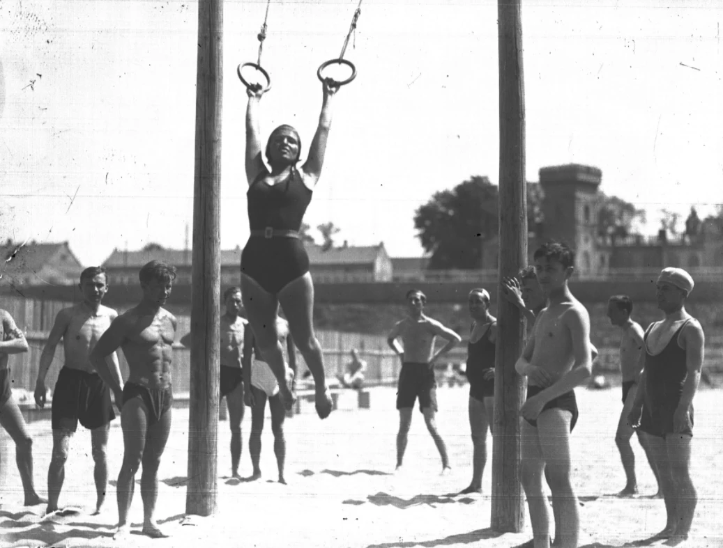 Kobieta na huśtawce oraz inni plażowicze podczas zabawy i wypoczynku. Plaża Towarzystwa Uniwersytetu Robotniczego w Krakowie (zdjęcie z 1931 roku)