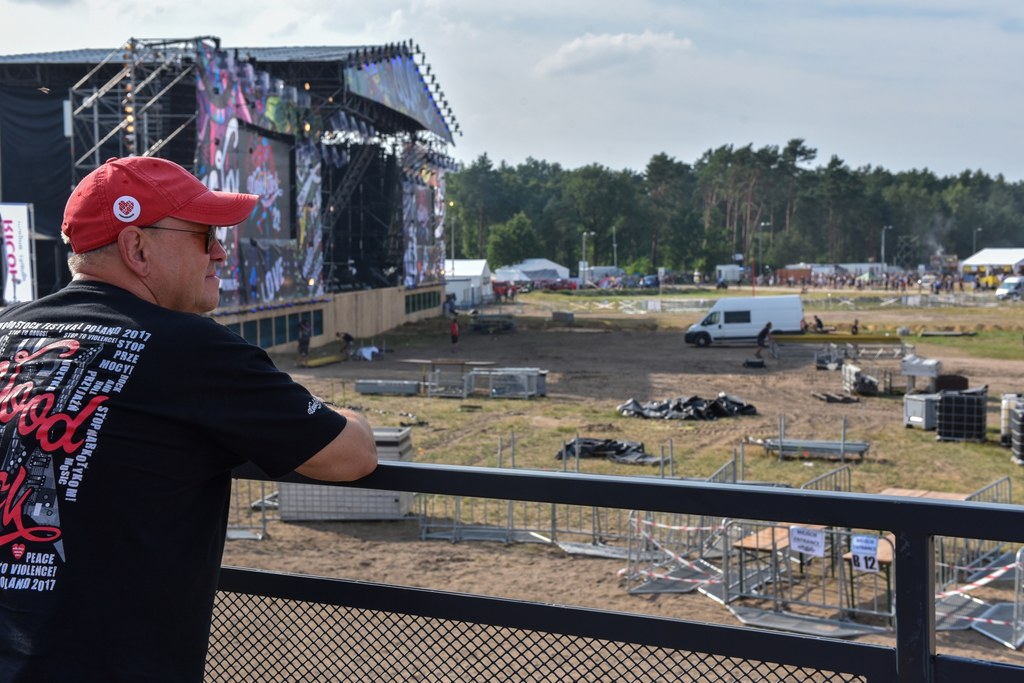 Jurek Owsiak patrzy na ogrodzone barierkami pole przed Dużą Sceną Przystanku Woodstock