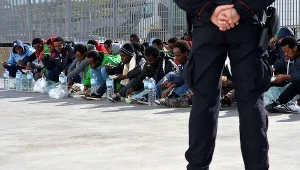 Włoski policjant pilnuje migrantów na Lampedusie