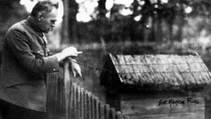 Józef Piłsudski pali papierosa oparty o płot i obserwuje ul w Sulejówku