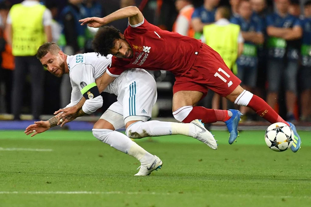 Obrońca Realu Madryt Sergio Ramos przytrzymuje Mohameda Salaha. Gwiazda Liverpoolu przypłaciła to starcie kontuzją Obrońca Realu Madryt Sergio Ramos przytrzymuje Mohameda Salaha. Gwiazda Liverpoolu przypłaciła to starcie kontuzją