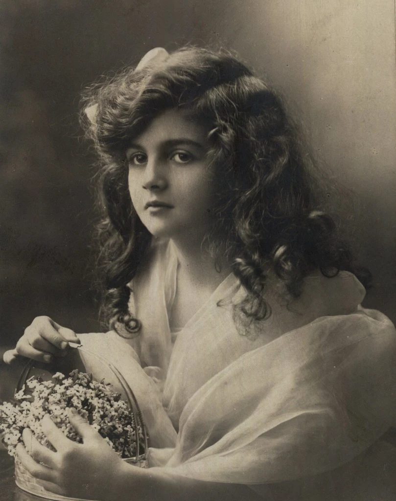 Dziewczyna z koszyczkiem kwiatków. Fotografia z początku XX wieku (domena publiczna)