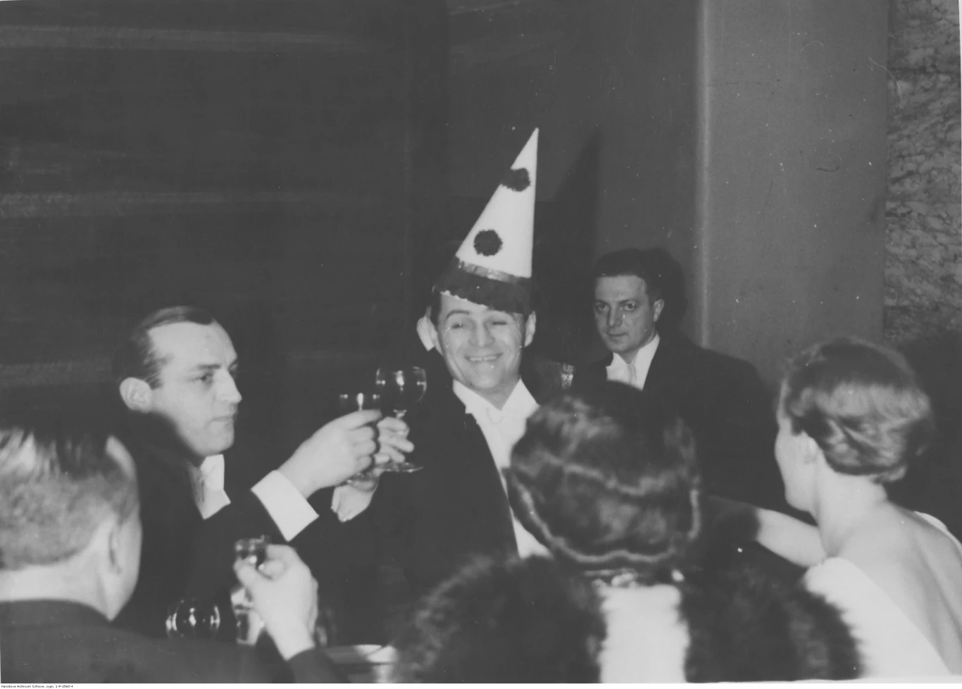 Bal sylwestrowy w lokalu Adria w Warszawie. Grupa uczestników balu podczas wznoszenia toastu noworocznego. Widoczni m.in. aktorzy: Adolf Dymsza (w czapce) i Tadeusz Olsza (z lewej)