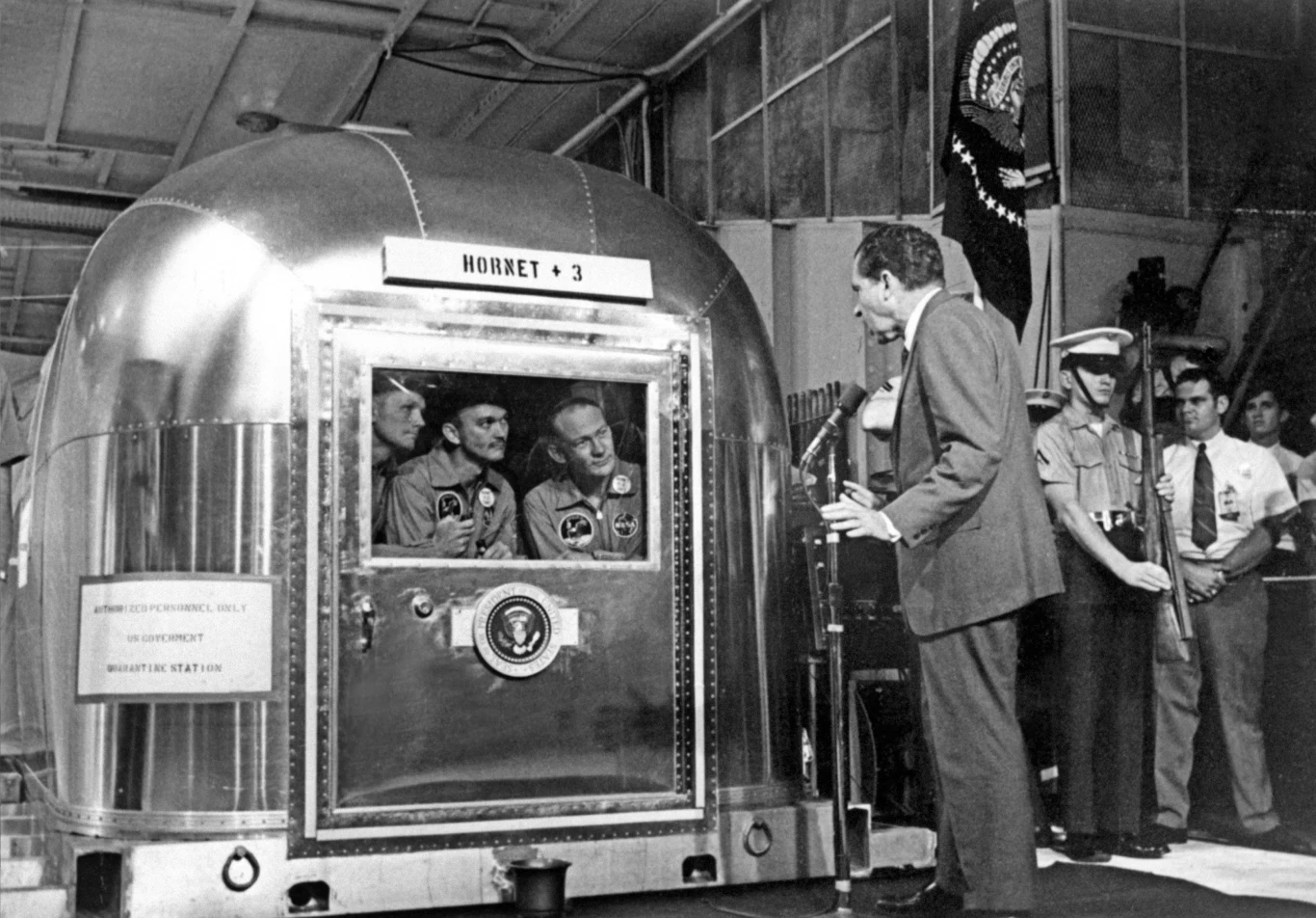 Prezydent Nixon odwiedza załogę Apollo 11 podczas trwającej 21 dni kwarantannie. Na kilka dni przed starem misji NASA przygotowała specjalne reguły dotyczące ewentualnego kontaktu z życiem pozaziemskim. Zakładały one, że astronauci muszą przejść szczegółowe badania i kwarantannę na wypadek, gdyby ich organizm został zarażony patogenem kosmicznego pochodzenia. Na szczęście tak się nie stało.