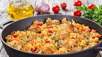 Paella z ryżem i kurczakiem

Składniki na 4-6 porcji: 4-6 pałeczek kurczaka, 30 dag wędzonego boczku, 30 dag ryżu, 2 duże cebule, 3 papryki (czerwona, żółta i zielona),  1 litr bulionu, 1 szklanka mrożonego groszku, 3-4 ząbki czosnku, 6 łyżek oleju, 1 łyżeczka ostrej papryki w proszku, szczypta kurkumy, sól,  pieprz.

Papryki dokładnie oczyścić z nasion, miąższ pokroić w paski. Cebule pokroić w kostkę, czosnek posiekać. Na patelni rozgrzać 4 łyżki oleju. Pałeczki z kurczaka umyć, osuszyć, posypać pieprzem i solą, kłaść na gorącym oleju, obsmażyć na złoty kolor.

Do kurczaka dodać cebulę, czosnek i chwilę podsmażyć. Dorzucić kawałki papryki. Do podsmażonych pałeczek z warzywami wsypać ryż, kurkumę, sól, pieprz, dolać gorący bulion. Gotować, aż ryż wchłonie prawie cały płyn.

Dziesięć minut przed końcem dodać groszek i gotować, aż groszek będzie miękki. Boczek pokroić w słupki i usmażyć na rumiano na pozostałych 2 łyżkach oleju i obłożyć nim paellę.