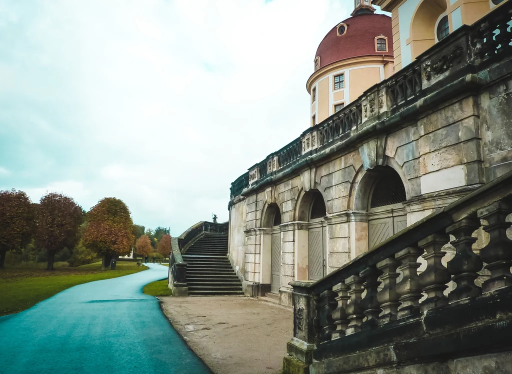 Wokół pałacu założony został rozległy barokowy park ze stawami, na który rozciąga się oszałamiający widok z wielkiego tarasu. Jest w nim bażanciarnia, w której hodowano ptaki na zamkowe uczty, miniaturowy port z fałszywą latarnią morską i małym molo. Pałac Moritzburg do końca II wojny zamieszkiwał książę Ernst Heinrich von Sachsen. Gdy opuszczał zamek przed nadchodzącą Armią Czerwoną, nakazał zapakowanie cennych przedmiotów w solidne skrzynie i zakopanie ich w parku. Skarby miały czekać na powrót arystokraty. Nie doczekały się, bo zostały niemal w całości odnalezione przez żołnierzy. Kilka brakujących pakunków odnaleźli 10 lat temu niemieccy poszukiwacze. Dziś każdy może w Moritzburgu liczyć na odnalezienie skarbu – nastroju i atmosfery oraz pięknych zdjęć, jakie z tej pięknej rezydencji można przywieźć. Tekst: Marcin Jamkowski, Świat i Ludzie Wokół pałacu założony został rozległy barokowy park ze stawami, na który rozciąga się oszałamiający widok z wielkiego tarasu. Jest w nim bażanciarnia, w której hodowano ptaki na zamkowe uczty, miniaturowy port z fałszywą latarnią morską i małym molo. Pałac Moritzburg do końca II wojny zamieszkiwał książę Ernst Heinrich von Sachsen. Gdy opuszczał zamek przed nadchodzącą Armią Czerwoną, nakazał zapakowanie cennych przedmiotów w solidne skrzynie i zakopanie ich w parku. Skarby miały czekać na powrót arystokraty. Nie doczekały się, bo zostały niemal w całości odnalezione przez żołnierzy. Kilka brakujących pakunków odnaleźli 10 lat temu niemieccy poszukiwacze. Dziś każdy może w Moritzburgu liczyć na odnalezienie skarbu – nastroju i atmosfery oraz pięknych zdjęć, jakie z tej pięknej rezydencji można przywieźć. Tekst: Marcin Jamkowski, Świat i Ludzie