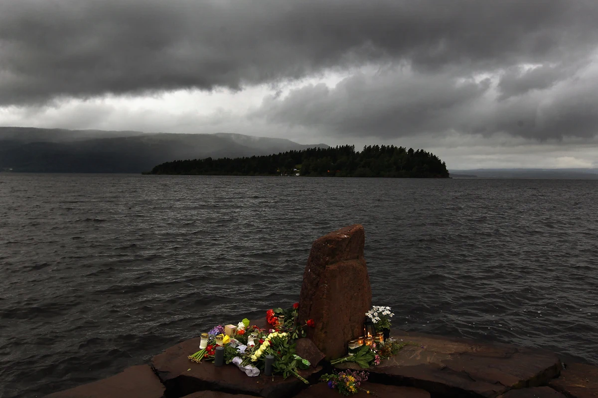 W idok na wyspę Utoya. Na brzegu kwiaty złożone dla uczczenia pamięci ofiar W idok na wyspę Utoya. Na brzegu kwiaty złożone dla uczczenia pamięci ofiar