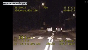 Kierowca wyprzedzający inny samochód na pasach, na podwójnej linii ciągłej. Nagranie z kamery w umieszczonej w radiowozie.