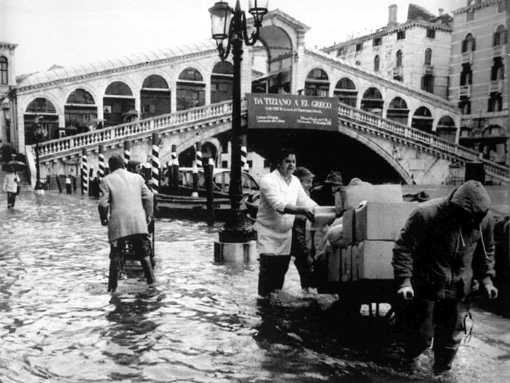 Pracownicy pobliskich hoteli próbują zabezpieczyć bagaże swoich gości. W tle słynny most Rialto. Wenecja, 1981 rok. Pracownicy pobliskich hoteli próbują zabezpieczyć bagaże swoich gości. W tle słynny most Rialto. Wenecja, 1981 rok.