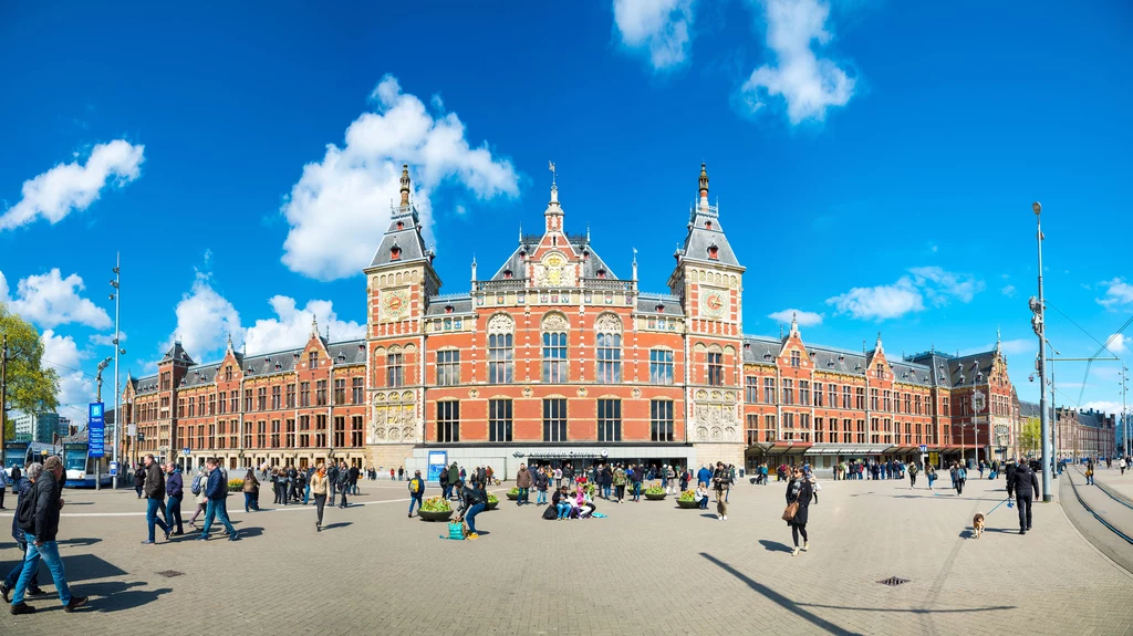 Podróżni przyjeżdżający do Amsterdamu pociągiem wchodzą w mury bogato zdobionego dworca