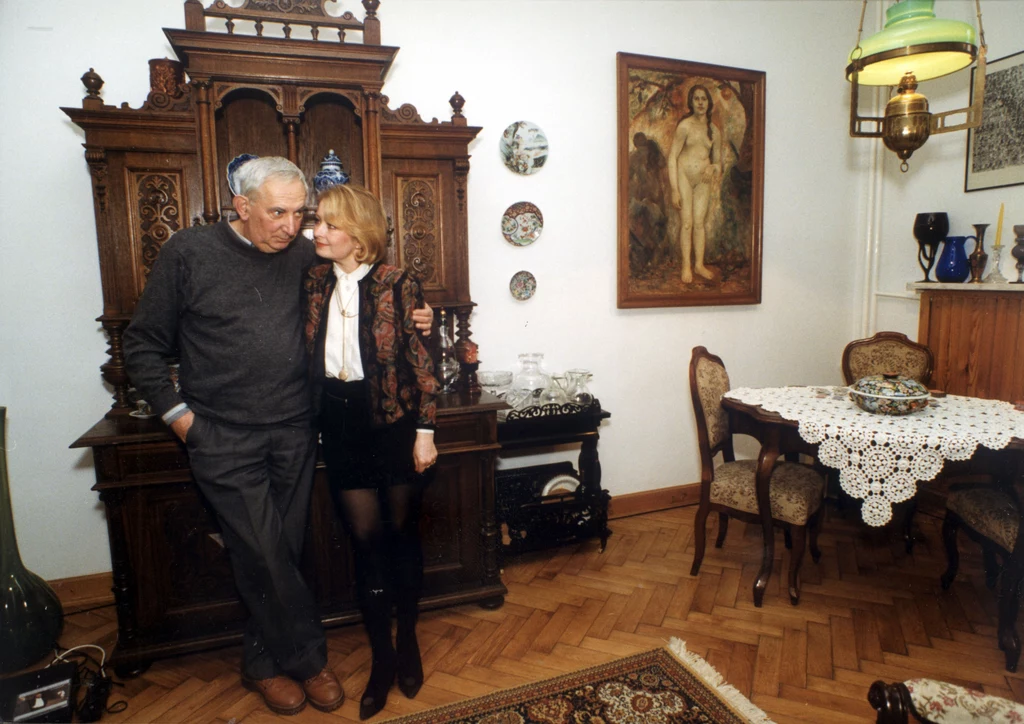 Magdalena Zawadzka i Gustaw Holoubek Do mieszkania przy Narbutta 53 w przedwojennej kamienicy na warszawskim Mokotowie aktorskie małżeństwo wprowadziło się na początku lat 80. Postawili na tradycję. Urządzili je po mieszczańsku, z pięknymi meblami, obrazami i bibelotami, co okazało się stylem uniwersalnym – tak samo dobrym dawniej, jak dziś. Elementem takiego wystroju jest komoda. Królowała w domach naszych babć i nadal jest modna. Pasuje do każdego wnętrza. Ma wiele zastosowań, pojemne szuflady pozwalają przechowywać pościel, dokumenty, zdjęcia. Poza praktyczną pełni też funkcję dekoracyjną umożliwiając ustawienie przedmiotów, do których mamy sentyment: fotografii, figurek, bibelotów. Podłogi mieszkania pokrywa dębowy parkiet „w jodełkę” dodający pomieszczeniom klasy i smaku. Na zdjęciu. Gustaw Holoubek z Magdaleną Zawadzką - rok 1992 Magdalena Zawadzka i Gustaw Holoubek Do mieszkania przy Narbutta 53 w przedwojennej kamienicy na warszawskim Mokotowie aktorskie małżeństwo wprowadziło się na początku lat 80. Postawili na tradycję. Urządzili je po mieszczańsku, z pięknymi meblami, obrazami i bibelotami, co okazało się stylem uniwersalnym – tak samo dobrym dawniej, jak dziś. Elementem takiego wystroju jest komoda. Królowała w domach naszych babć i nadal jest modna. Pasuje do każdego wnętrza. Ma wiele zastosowań, pojemne szuflady pozwalają przechowywać pościel, dokumenty, zdjęcia. Poza praktyczną pełni też funkcję dekoracyjną umożliwiając ustawienie przedmiotów, do których mamy sentyment: fotografii, figurek, bibelotów. Podłogi mieszkania pokrywa dębowy parkiet „w jodełkę” dodający pomieszczeniom klasy i smaku. Na zdjęciu. Gustaw Holoubek z Magdaleną Zawadzką - rok 1992