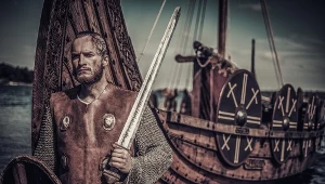 Rekonstruktor przebrany za wikińskiego wojownika na tle drakkaru, czyli słynnej długiej łodzi