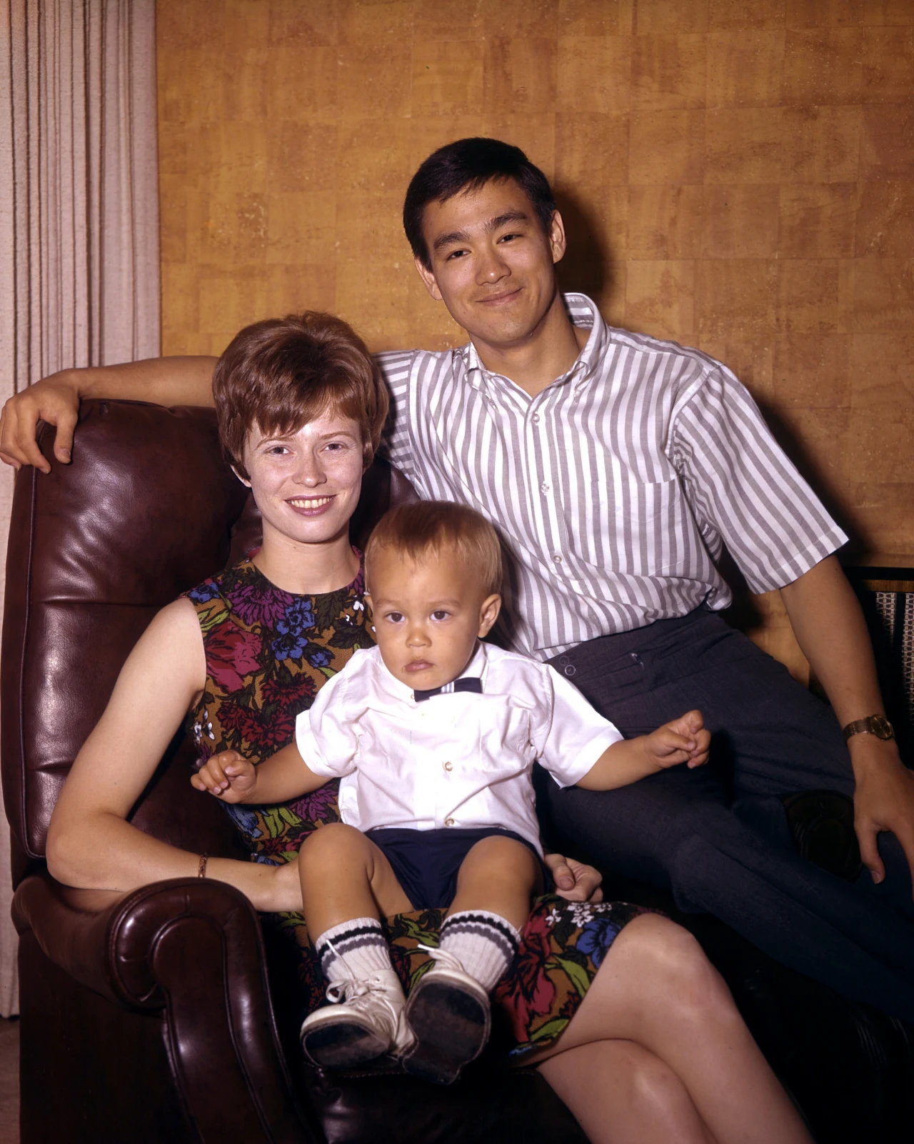 Brandon Lee na kolanach u mamy. Na fotelu siedzi ojciec - Bruce Lee