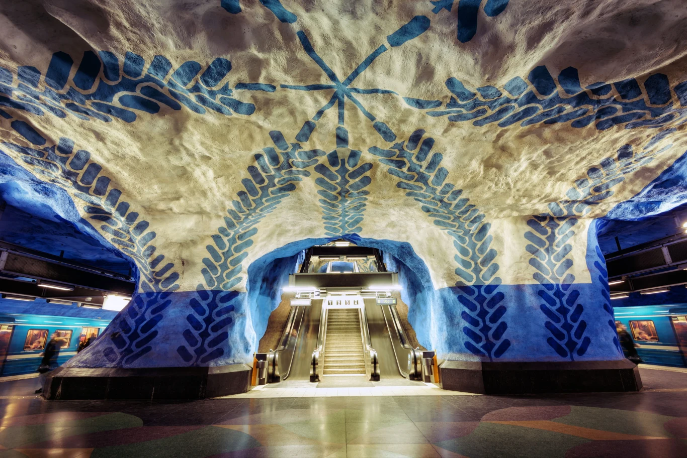 Sztokholmskie metro zostało zaprojektowane w taki sposób, aby spełniało jednocześnie funkcję transportu publicznego i umożliwiało ludziom kontakt ze sztuką. W końcu to tutaj każdego dnia przewijają się tysiące zmęczonych mieszkańców – dlaczego nie umilić im w ten sposób podróży i pozwolić na obcowanie z czymś pięknym? Na zdjęciu: T-centralen - główna stacja miasta, którą przecinają wszystkie linie. Możemy tutaj podziwiać piękne, biało-niebieskie malowidła z żółtymi elementami, autorstwa Pera Olofa Ultvedta. 
