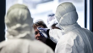 Służby w kombinezonach ochronnych mierzą temperaturę, zdjęcie ilustracyjne