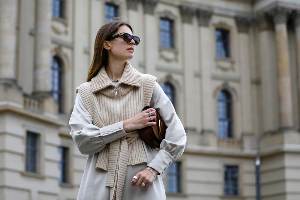  Jacqueline Zelwis ma na sobie długą beżową sukienkę Black Palms, beżową kamizelkę Holzweiler, brązową torebkę Polo Ralph Lauren i okulary Bottega Veneta.